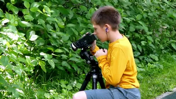 Menino com câmera de vídeo dispara filme sobre a natureza do parque verde fundo . — Vídeo de Stock