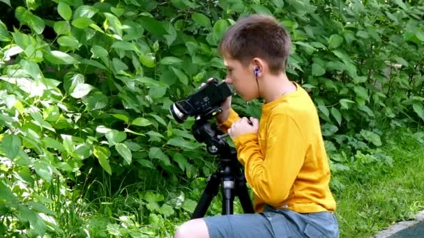 Jeune garçon avec caméra vidéo tourne un film sur la nature du fond vert du parc . — Video