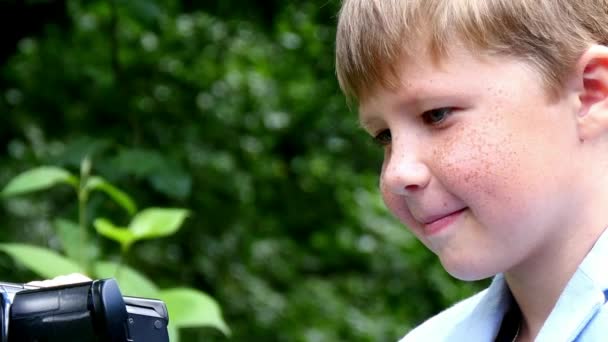 Молодий хлопчик з відеокамерою знімає фільм про природу фону зеленого парку . — стокове відео