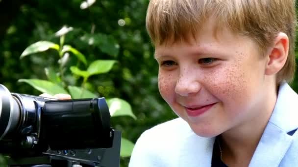 Menino com câmera de vídeo dispara filme sobre a natureza do parque verde fundo . — Vídeo de Stock