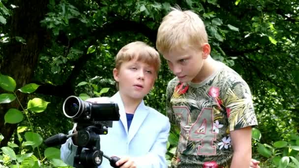 ビデオカメラを持った若い男の子が緑豊かな公園の背景の性質について映画を撮影します。. — ストック動画