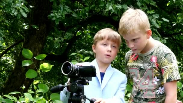 Niños jóvenes con cámara de vídeo filma película sobre la naturaleza del fondo verde del parque . — Vídeo de stock
