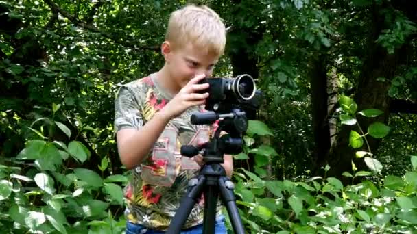 Jeune garçon avec caméra vidéo tourne un film sur la nature du fond vert du parc . — Video