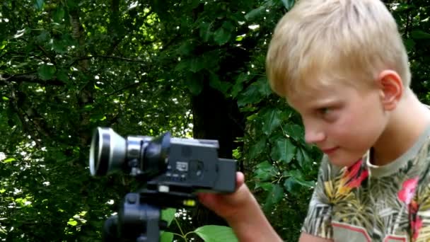 비디오 카메라와 함께 어린 소년 쏘고 녹색 공원 배경의 자연에 대 한 영화. — 비디오