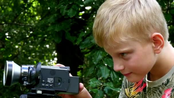 Niño con cámara de vídeo filma película sobre la naturaleza del fondo verde del parque . — Vídeos de Stock