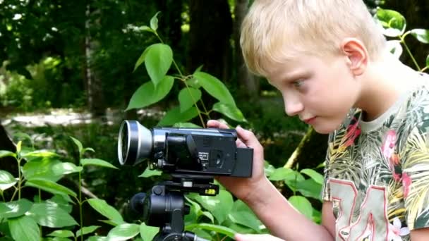 Menino com câmera de vídeo dispara filme sobre a natureza do parque verde fundo . — Vídeo de Stock