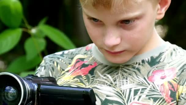 Giovane ragazzo con videocamera scatta film sulla natura del parco verde sfondo . — Video Stock