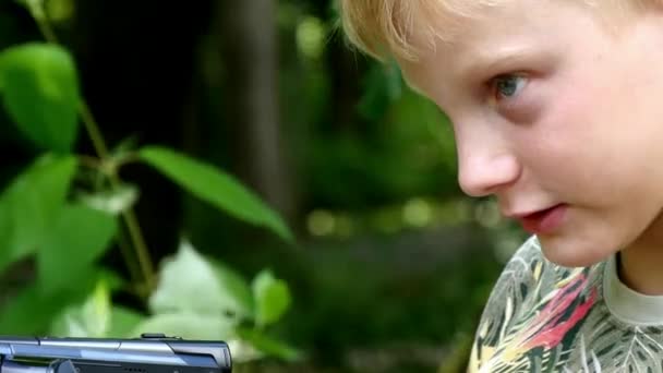 ビデオ カメラの少年は 緑豊かな公園の背景の性質についての映画を撮影します 夏の屋外子供たちは 映画の創造的な仕事です 美しい映像 子供の頃に世界を見て興味深い — ストック動画