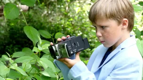 Młody chłopak z kamerą wideo strzela film o charakter tło zielony park. — Wideo stockowe