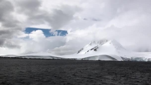 Κύματα και σύννεφα στο παρασκήνιο του χιονιού βράχου στον ωκεανό της Ανταρκτικής. — Αρχείο Βίντεο
