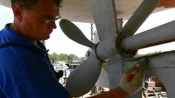 Trabajador pinta metal de vieja hélice de barco oxidado en astillero en puerto . — Vídeo de stock