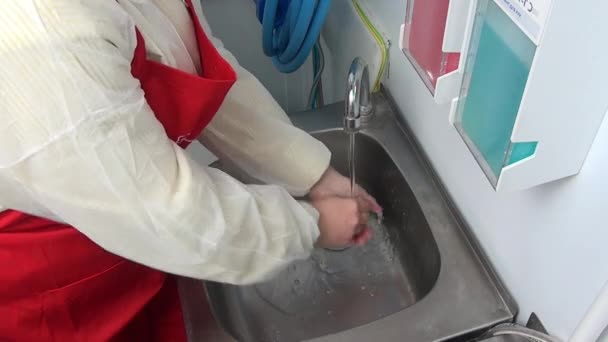 女工在红色围裙洗她的手在水龙头之下. — 图库视频影像