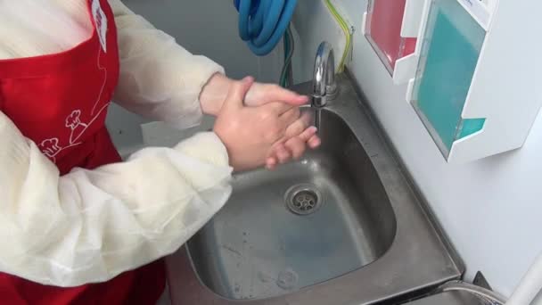 Kvinna arbetare i rött förkläde tvättar händerna under kranen. — Stockvideo