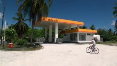 Kadın bir benzin istasyonuna yolda bir bisiklet sürme.