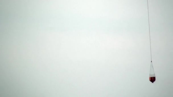 Rode opknoping scoop vanuit een brand helikopter voert water op grijze hemelachtergrond. — Stockvideo