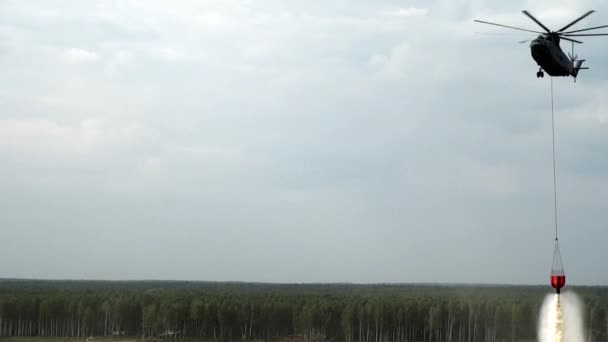 Red hanging scoop from a fire helicopter dumps water on gray sky background. — Stock Video