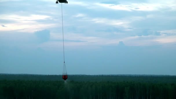 Red hanging scoop from a fire helicopter dumps water on gray sky background. — Stock Video