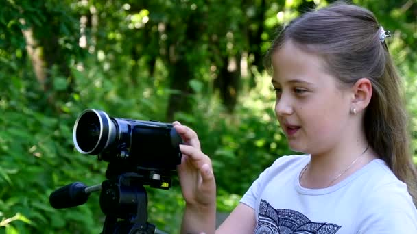 ビデオカメラを持つ少女は、スローモーションの緑豊かな公園の自然の中映画を撮影します。. — ストック動画