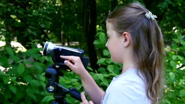 Chica joven con cámara de vídeo dispara películas en la naturaleza en el parque verde de cámara lenta . — Vídeos de Stock