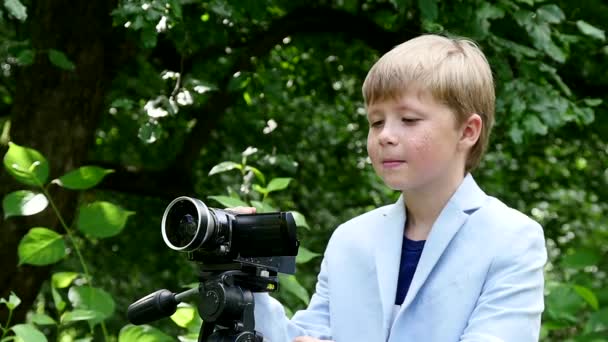 Niño con cámara de vídeo filma película sobre la naturaleza en el parque verde de cámara lenta . — Vídeo de stock