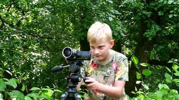 Jeune garçon avec caméra vidéo tourne le film dans la nature du parc vert au ralenti . — Video