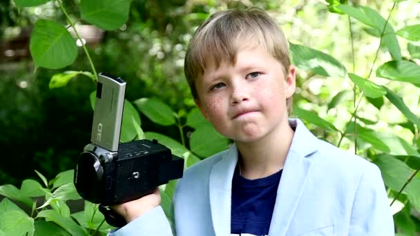 Jeune garçon avec caméra vidéo tourne le film dans la nature du parc vert au ralenti . — Video