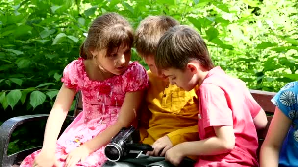 緑豊かな公園のスローモーションでベンチにビデオカメラで子供 若い男の子と女の子の夏の屋外は 映画の創造的な仕事です 美しい映像 子供の頃に世界を見て興味深い — ストック動画