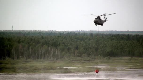 Грузовой пожарный вертолет с подвешенным ковшем забирает воду из резервуара . — стоковое видео