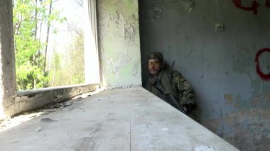 Yok edilmiş bir evde bir silah ile askeri üniformalı asker durumdadır.