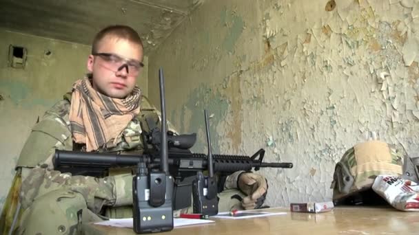O soldado no uniforme militar com a arma está perto de uma janela da casa arruinada . — Vídeo de Stock