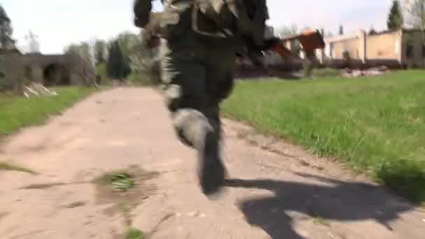 Voják v uniformě vojenských zbraní, které běží na pozadí zničeného domu. — Stock video