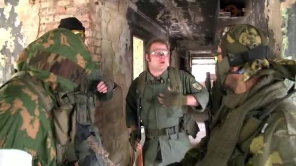 Menschen in Militäruniform mit Waffen reden in zerstörtem Haus. — Stockvideo