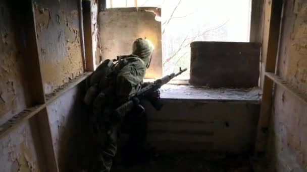 Soldado em uniforme militar com uma arma está em posição em uma casa destruída . — Vídeo de Stock