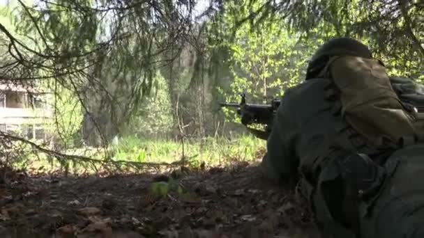 Mann in Militäruniform mit Waffe versteckt sich unter Baum. — Stockvideo