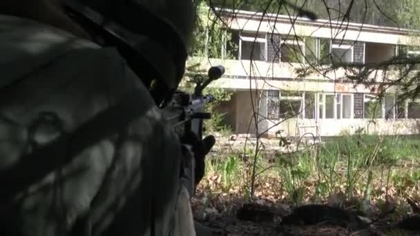 Man in military uniform with a weapon hides under tree. — Stock Video