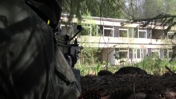 Muž ve vojenské uniformě se zbraní skrývá pod stromem. — Stock video