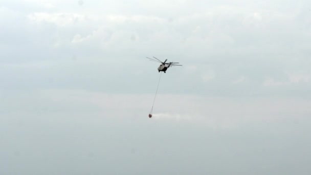 Σέσουλα κόκκινο κρέμεται από ένα ελικόπτερο Πυροσβεστική χωματερές νερό σε φόντο γκρίζο ουρανό. — Αρχείο Βίντεο