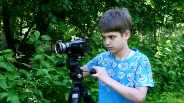 Genç oğlan video kameraya yeşil park arka plan üzerinde görünüyor..