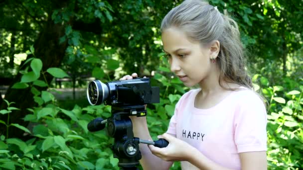 Jong meisje kijkt naar videocamera op achtergrond van groene park achtergrond. — Stockvideo