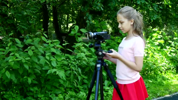 Giovane ragazza guarda in videocamera su sfondo di sfondo verde parco . — Video Stock