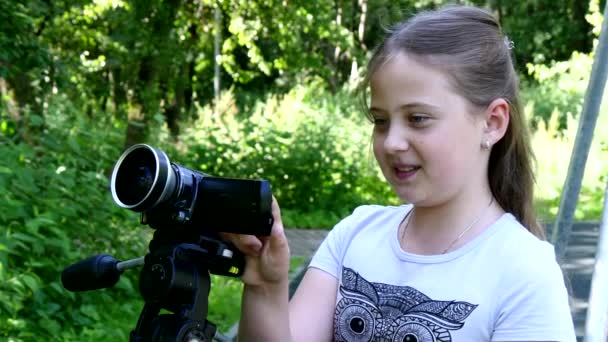 Young girl looks into video camera on background of green park background. — Stock Video
