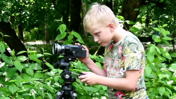 Niño con cámara de vídeo filma película sobre la naturaleza del fondo verde del parque . — Vídeo de stock
