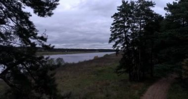 Arka planda gökyüzü ve büyüleyici manzara manzaralı bulutlarla çevrili bir nehir üzerinde evleri ve bahçeleri olan kırsal bir manzara. Açık hava iklimi kavramı.