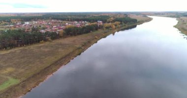 Arka planda gökyüzü ve büyüleyici manzara manzaralı bulutlarla çevrili bir nehir üzerinde evleri ve bahçeleri olan kırsal bir manzara. Açık hava iklimi kavramı.