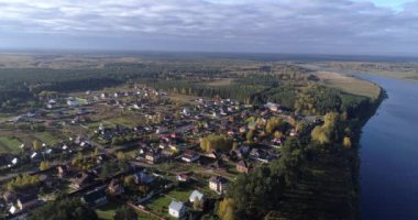 Arka planda gökyüzü ve büyüleyici manzara manzaralı bulutlarla çevrili bir nehir üzerinde evleri ve bahçeleri olan köyün hava manzaralı manzarası. Açık hava iklimi kavramı.