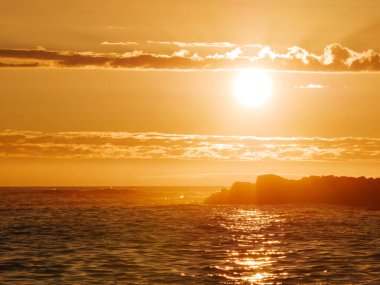 Portekiz 'de okyanusta yaz günbatımı. Sudaki yansımalar ve siluetteki kayalık ada.