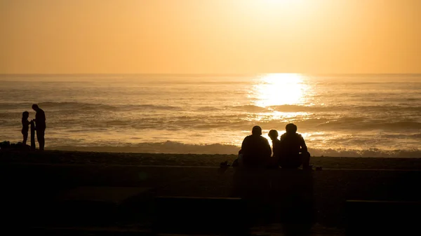 Family in silhouette at the beach watching the beautiful sunset. Unidentifiable people.