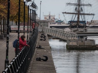 Dublin rıhtımlarının ilerisindeki kıtlık gemisine ve Dublin rıhtımına bakın. Ekim 'de bulutlu bir gün. Telefonda nehre bakan tanımlanamayan bir kişi var..