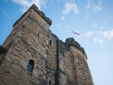Newcastle Castle Keep in Newcastle upon Tyne, England. View from below at an angle with British flag flying at top of the keep and blue sky with clouds. clipart
