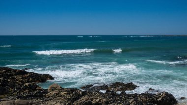 Portekiz 'deki doğal kayalık plajı. Parlak bir yaz gününde dalgalar kayalara çarpıyor..